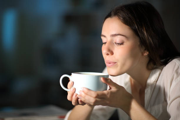 frau bläst zu kühlen heißen kaffee in der nacht zu hause - caffeine free stock-fotos und bilder