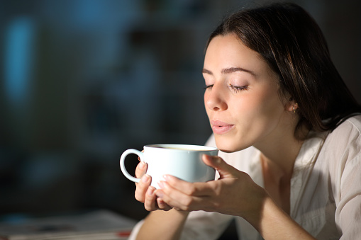 Woman blowing to cool hot coffee in the night at home