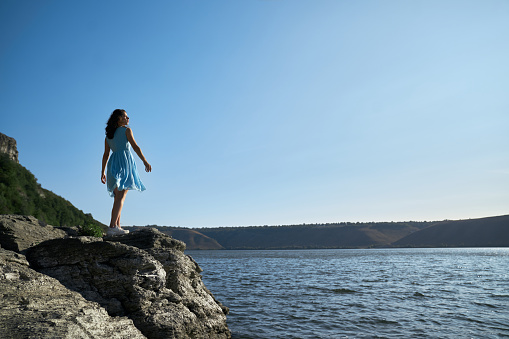 a woman looking at the horizon in a blue dress touching the texture of wooden railing