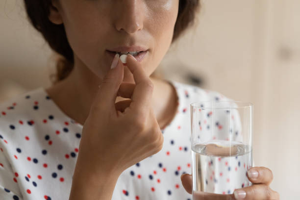 giovane donna tenere il bicchiere d'acqua prepararsi a deglutire pillola - painkiller pill capsule birth control pill foto e immagini stock