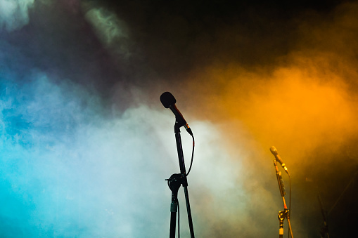 Silhouette of a microphone on an empty stage with coloured lighting and smoke effects