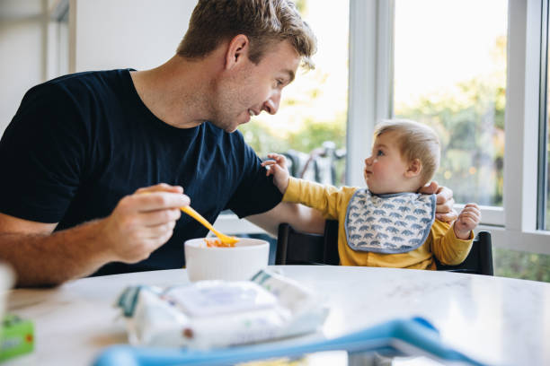 Man on paternity leave feeding his baby Caring father feeding food to his baby. Man on paternity leave taking care of his new born baby paternity stock pictures, royalty-free photos & images