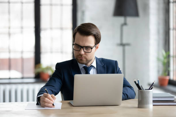 istock Confident businessman wearing glasses using laptop, writing notes 1308963226