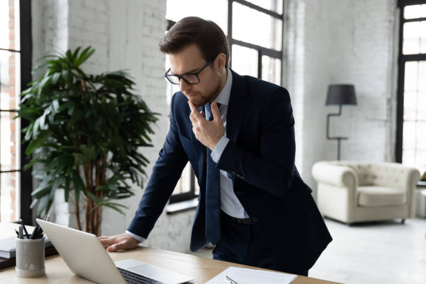 istock Thoughtful businessman pondering strategy, using laptop, standing near desk 1308963231