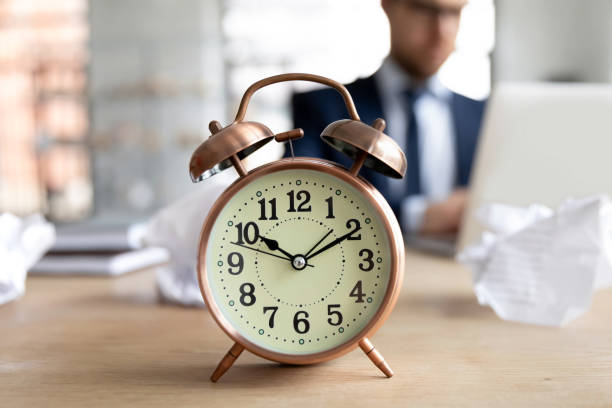 istock Close up clock standing on desk, busy businessman working 1308963285