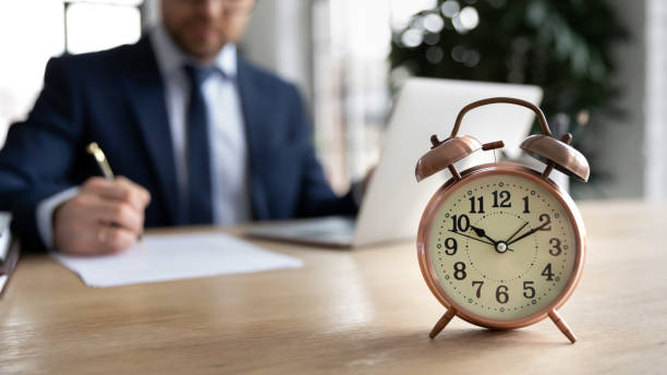 istock Close up alarm clock on desk, businessman working on background 1308963295