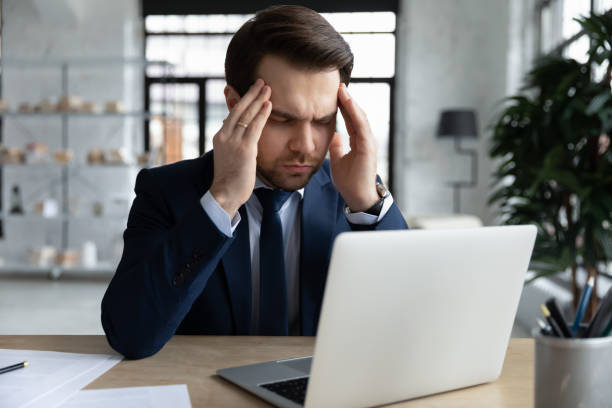 istock Tired stressed businessman touching temples, sitting at desk with laptop 1308963311