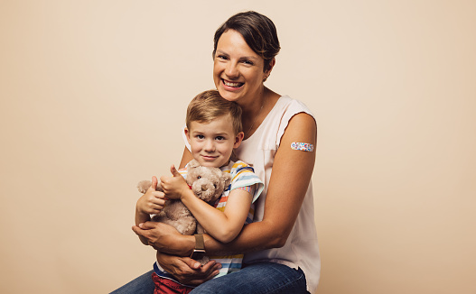 Portrait of carrying mother with her son after receiving a vaccine on arm. Mother and son with bandage on arm after getting immunity vaccine.