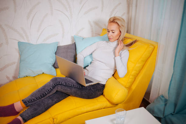 istock Happy smiling woman sitting on sofa and using laptop 1308968529