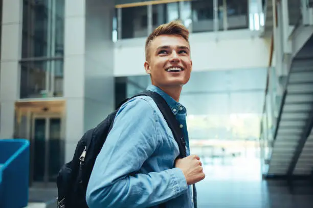 Young student with bag smiling in high school campus. Happy young man looking away and smiling after class.