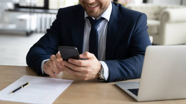 istock Close up successful smiling businessman using smartphone, sitting at desk 1308980541