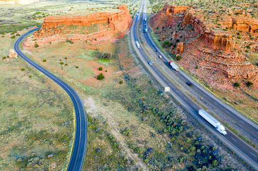 Road and highway between red rocks. Trucks speeding on Interstate 40 in New Mexico, USA, aerial view.