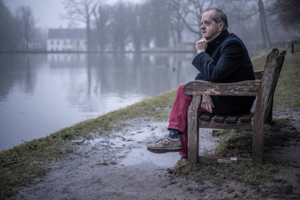 istock Sitting alone on a bench besides a lake, a middle aged man alone in misty forest, lonely and abandoned in gloomy atmospheric mood 1308983957