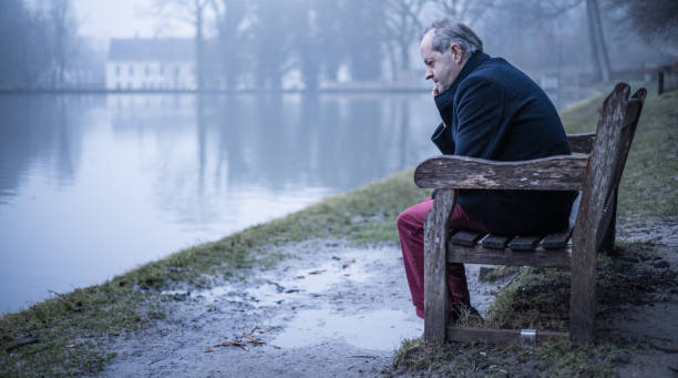 istock Having a headache while sitting on a park bench, a middle aged man alone in misty forest, lonely and abandoned in gloomy atmospheric mood 1308983984