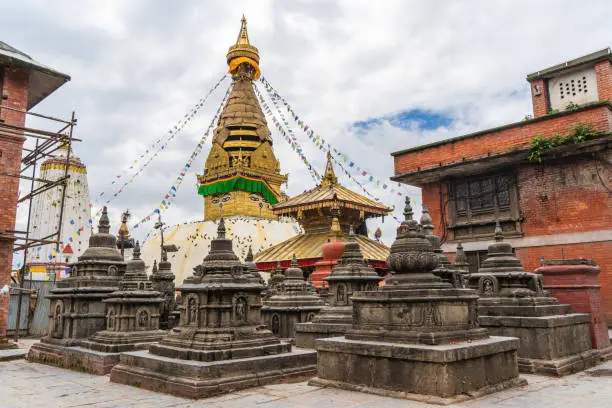 Stupa in Swayambhunath temple also called Monkey Temple, with traditional "Eyes of Buddha" painting on it and little stone stupas in foreground. Kathmandu city, travel in Nepal concept.