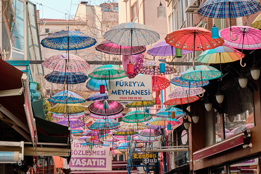 Turkey istanbul 01.03.2021. Many colorful and styled umbrellas hang on street in Kadikoy, moda istanbul with advertisement of tavern (meyhane)