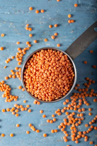 Red lentils in a metal measuring cup on a blue natural wood background. Top view.