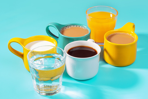 Multicolored mugs with drinks on a blue background side view.