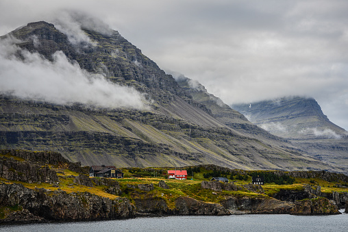 The cloud shrouded mountains of Berufjordur fjord tower above a farm near Djupivogur village on the East Fjords region of East Iceland.