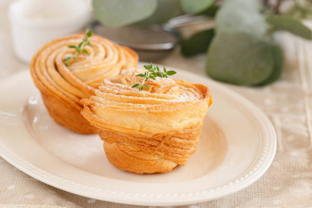 istock Homemade fresh baked cruffin sprinkle with icing or powdered sugar decorate with thyme leaf on white plate. Cruffin is a mixed of flaky layer croissant and muffin in muffin shape. Modern trend bakery. 1309017577