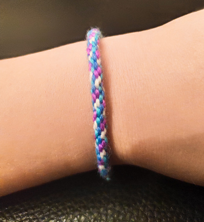 multi-colored bracelet made of threads on the arm, weaving from threads, needlework with children, sample, simple and cozy DIY decoration, cotton threads, color combination