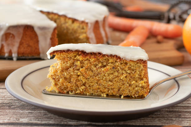 A piece of carrot cake Delicious and homemade baked carrot cake with almonds and lemon glaze. Served on a plate with cake served. Close up view. Whole cake is in the background carrot cake stock pictures, royalty-free photos & images