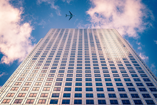 Highly detailed abstract wide angle view up towards the sky in the financial district of London City and its ultra modern contemporary building with unique architecture during a rare moment with commercial airplane passing / flying above the skyscraper. Shot on Canon EOS R full frame with 14mm wide angle prime premium lens. Image is ideal for business travel concepts background.