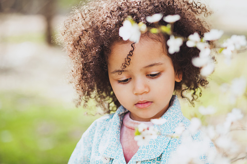 Outdoor portrait of cute little girl surrounded by blooming trees in springtime