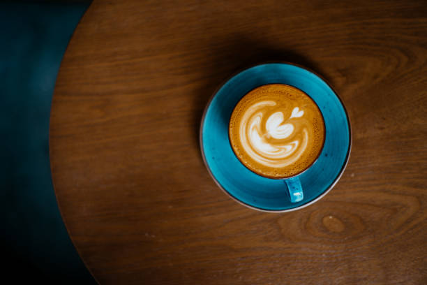 Flat white coffee in blue cup on top of wooden table Image of a flat white coffee with froth art in blue coffee cup on top of wooden table coffee table top stock pictures, royalty-free photos & images