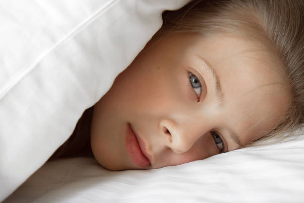 istock Girl peeking out from under the covers in bed 1309036557