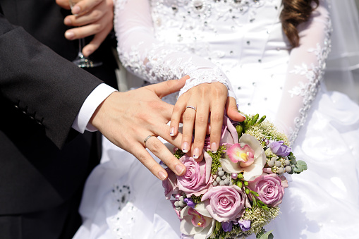 Hands of newlyweds with wedding rings on a bouquet of the bride.