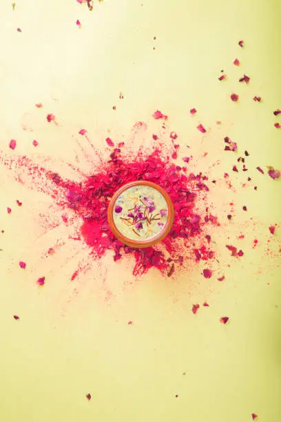 Photo of Indian Holi festival drink Thandai on a yellow background with a splash of colour. A traditional cold drink made using a mixture of milk, dry fruits, sugar and spices, garnished with saffron.