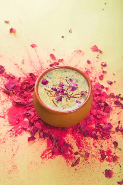 Photo of Indian Holi festival drink Thandai on a yellow background with a splash of colour. A traditional cold drink made using a mixture of milk, dry fruits, sugar and spices, garnished with saffron.