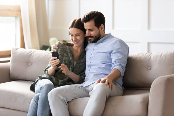 istock Smiling couple relax at home using smartphone gadget 1309039234