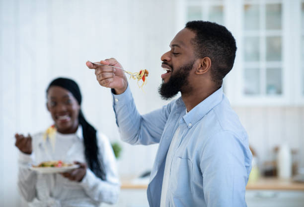 Cheerful Black Man Tasting Spaghetti While Having Lunch With Wife In Kitchen Cheerful Black Man Tasting Spaghetti While Having Lunch With Wife In Kitchen, Romantic African American Couple Enjoying Cooking And Eating Tasty Food At Home, Selective Focus On Guy spaghetti photos stock pictures, royalty-free photos & images