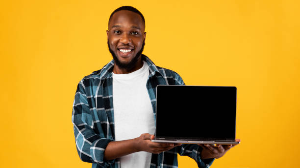 istock African Guy Showing Laptop Blank Screen On Yellow Background, Mockup 1309040167