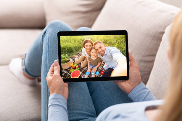 istock Young woman having remote conversation with happy family on picnic, using tablet computer at home 1309041770