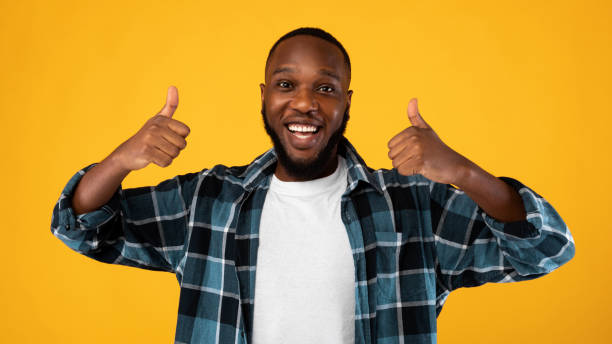 istock Black Man Gesturing Thumbs Up To Camera On Yellow Background 1309041885