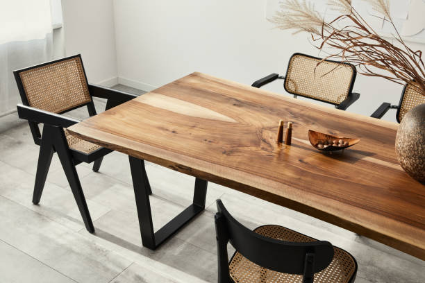 Interior design of stylish dining room interior with family wooden table, modern chairs, plate with nuts, salt and pepper shakers. Concrete floor. White wall. Template. Minimalist composition of dining room interior with wooden table, design chairs and elegant personal accessories. Template. dining table stock pictures, royalty-free photos & images