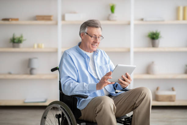 istock Joyful impaired senior man in wheelchair using tablet computer at home 1309042096