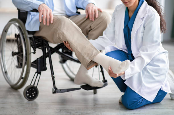 vista recortada del joven médico que revisa la pierna del paciente senior discapacitado durante una visita médica en casa - parálisis fotografías e imágenes de stock