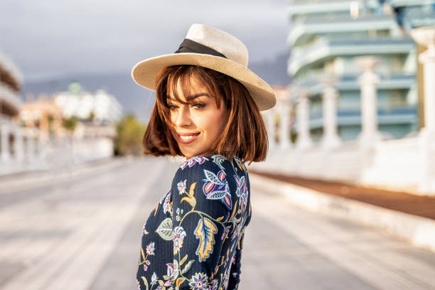 garota bonita sorridente usando chapéu de verão, olhando para a câmera enquanto caminhava na rua da cidade. - franja estilo de cabelo - fotografias e filmes do acervo