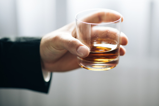 Man's hand holding glass of whiskey. Lonely man is addicted of alcohol.