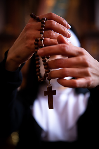 Nun lifting up wooden rosary beads, she is blurred in the background.