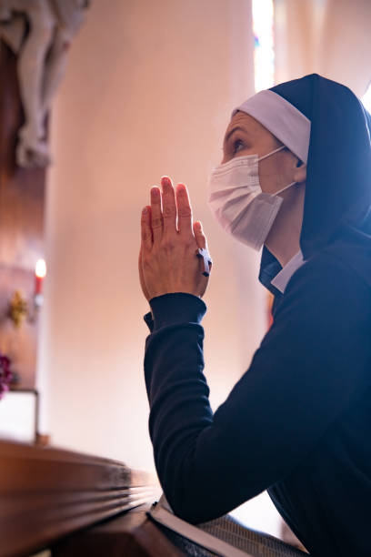 istock Nun praying in church, wearing protective face mask. 1309044502