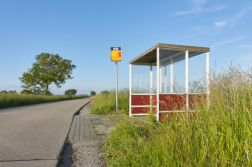Bus stop shelter with glass on a road in a rural area under a blue sky.
