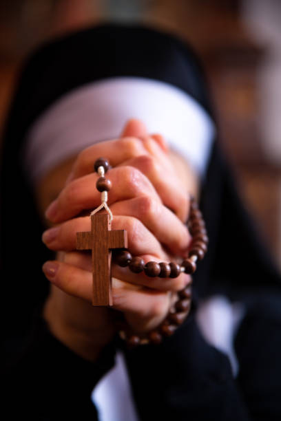 Close up on a nun holding rosary beads, praying. Nun holding hands together, praying to God, unrecognizable face, she is blurred in the background. nun praying cross human hand stock pictures, royalty-free photos & images