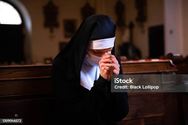 A Nun Bowing Her Head In Prayer Sitting In A Church Wearing Protective Face Mask Stock Photo - Download Image Now