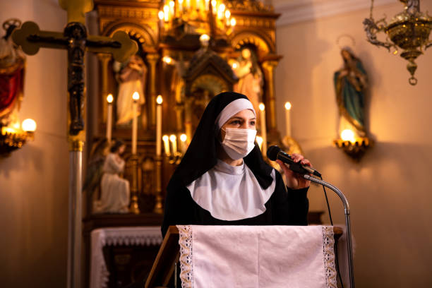 istock Nun talking on a microphone in Roman Catholic church wearing protective face mask. 1309046652