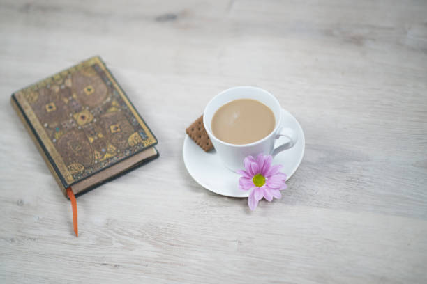istock A cup of coffee with pink flower and a book on white table. 1309046879